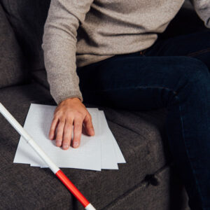 A close up of a man's hand reading braille documents on the couch